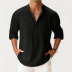 Cropped front view of a man wearing the shirt in black with a layered silver chain necklace and rolled sleeves.