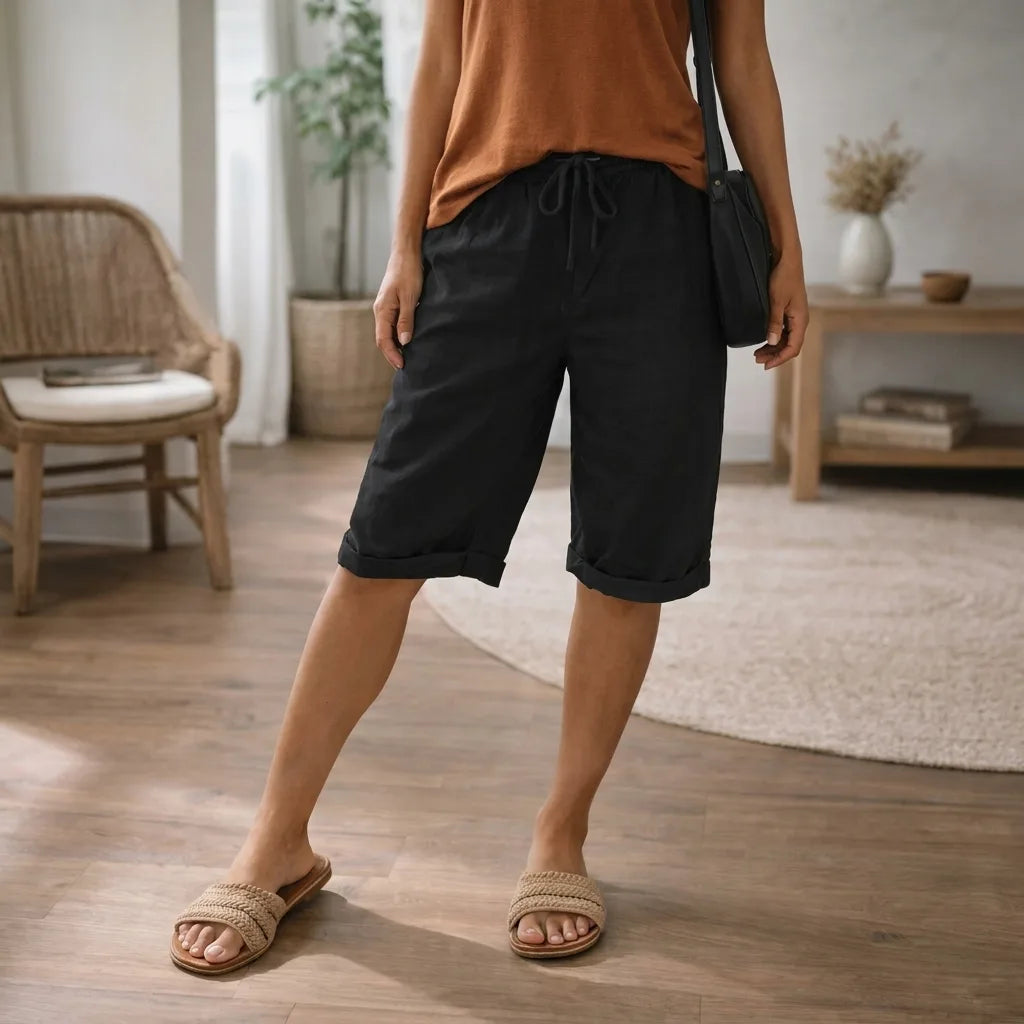 Black linen knee-length shorts with rolled cuffs and elastic drawstring waist, paired with a dark crossbody bag