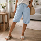 Light blue linen Bermuda shorts with cuffed hem and front drawstring, worn with a striped top and woven tote