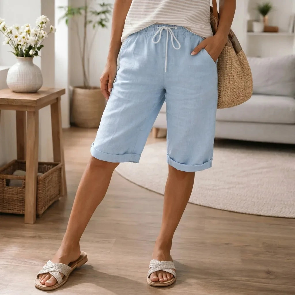 Light blue linen Bermuda shorts with cuffed hem and front drawstring, worn with a striped top and woven tote