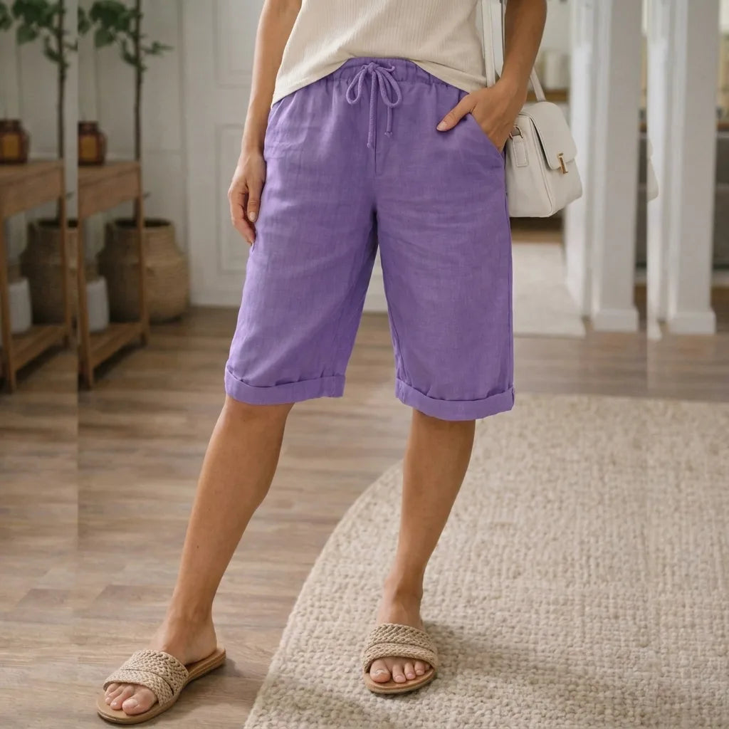Purple linen Bermuda shorts with cuffed leg and drawstring waistband, paired with a structured handbag