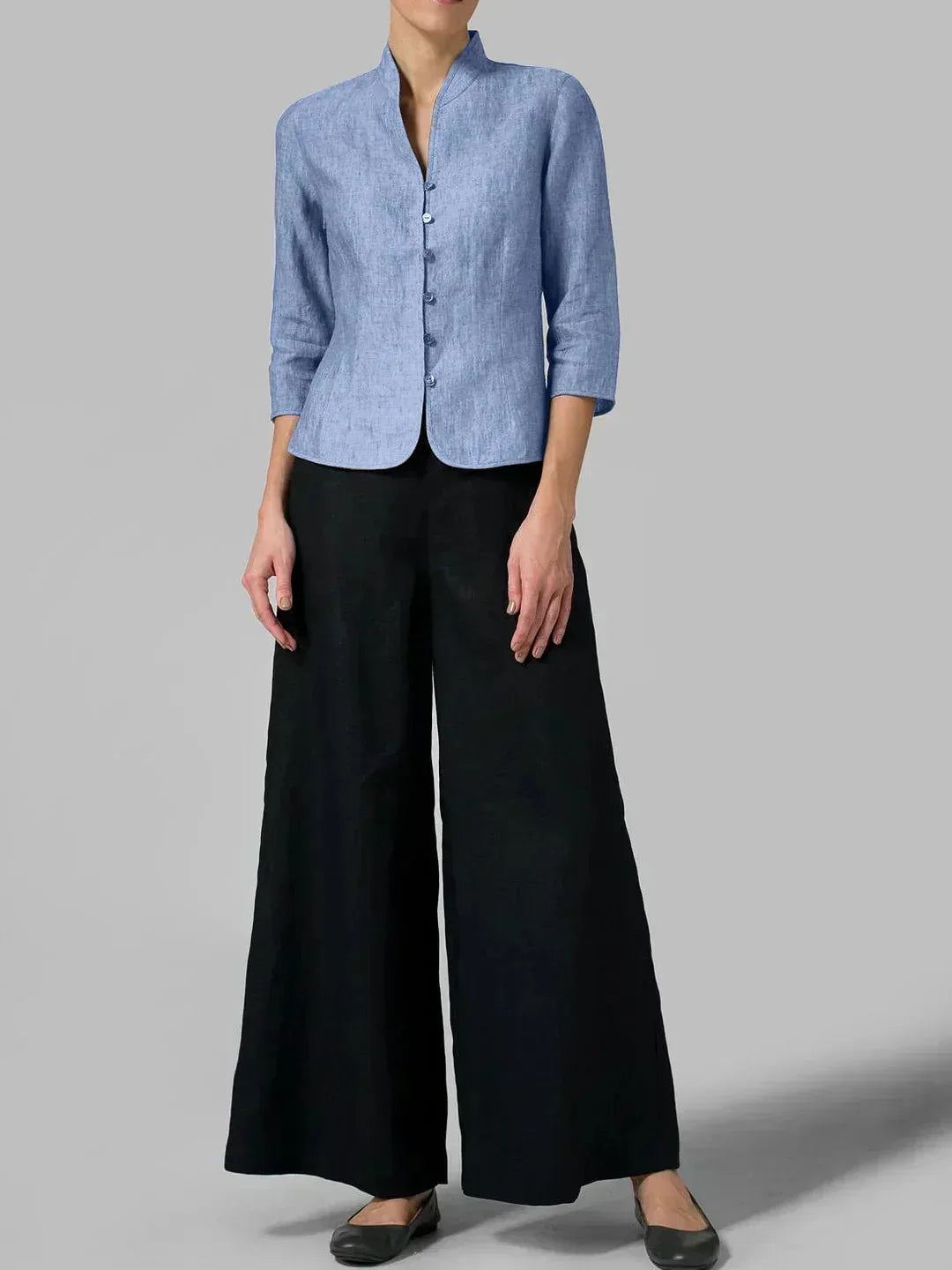 Full-length view of a light blue linen blazer worn with black wide-leg trousers, shown against a grey backdrop