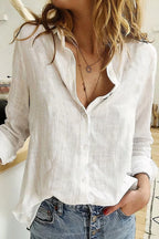 Close view of a white textured linen button-down blouse worn open at the collar with layered necklaces and jeans.