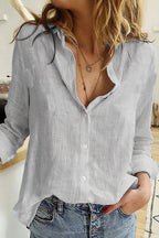 Light grey textured linen blouse with open collar and mother-of-pearl style buttons, worn with denim.