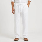 Close-up front view of white linen drawstring trousers paired with an open white linen shirt