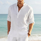 Man on the beach wearing a white linen Henley shirt with banded collar and rolled-up sleeves