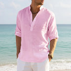 Man wearing a soft pink linen Henley shirt with rolled sleeves, standing against the ocean