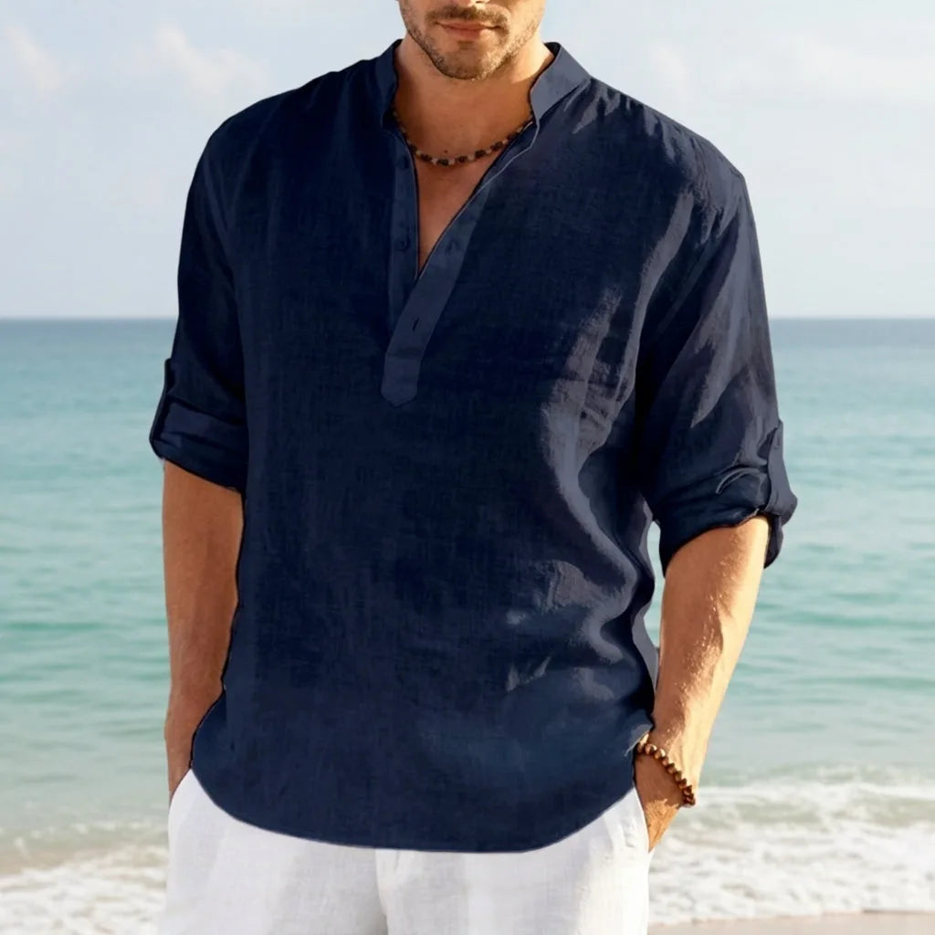 Man wearing a dark navy linen Henley shirt with rolled sleeves against a blurred seascape