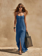 Side-angle shot of a mid-blue linen slip dress with scoop neckline and natural fabric drape to the floor