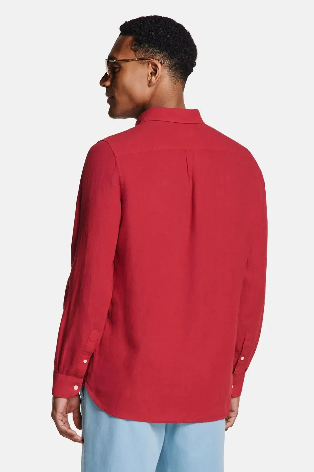 Back view of man in burgundy linen shirt paired with light blue trousers