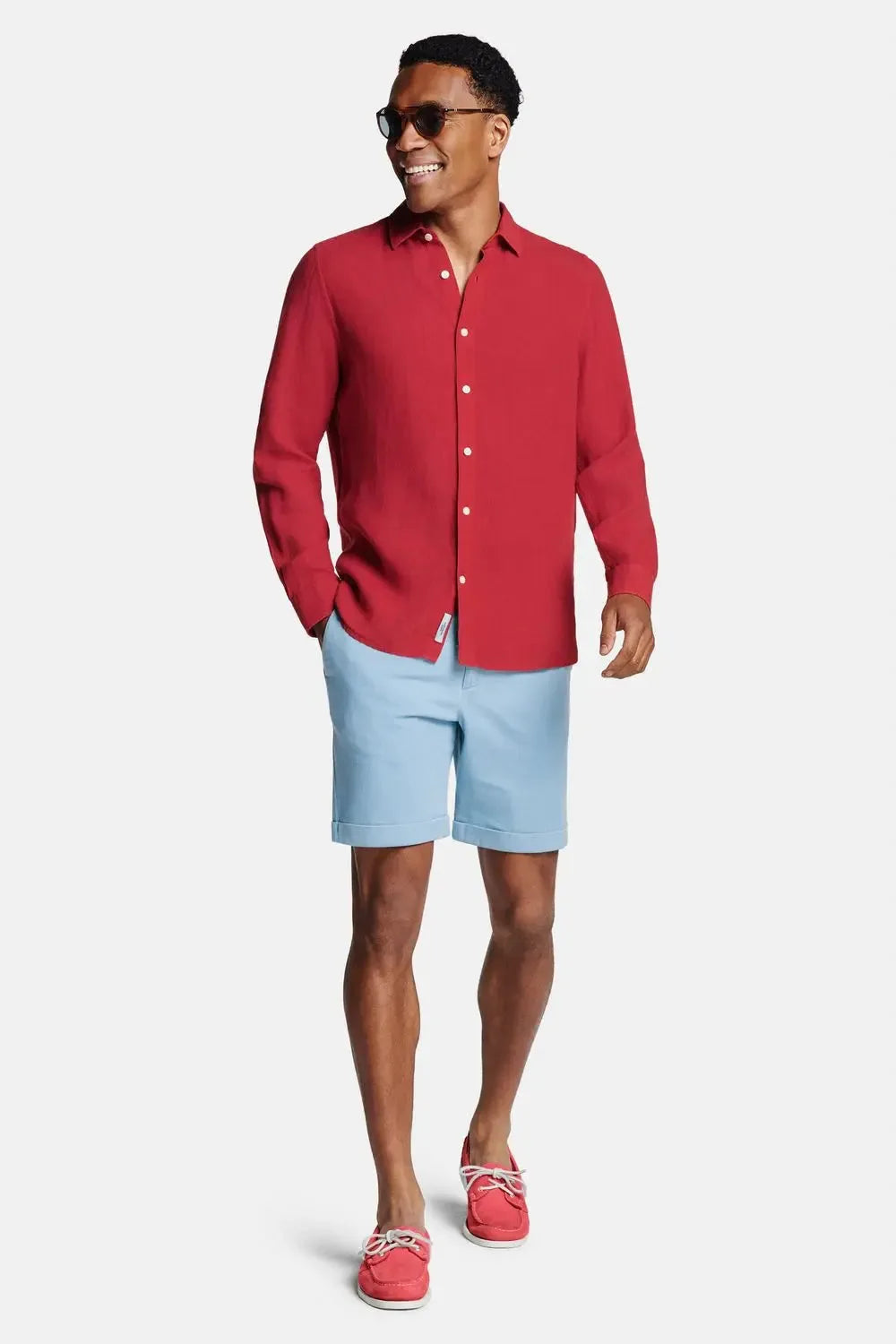 Full-length front view of model in burgundy linen shirt styled with light blue chino shorts and boat shoes