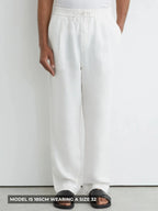 Front view of man wearing white relaxed-fit linen trousers with drawstring waist and black slide sandals