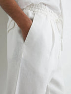 Close-up of hand in slanted side pocket showing white linen fabric texture and pleated waistband detail