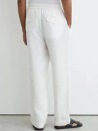 Back view of white linen trousers showing twin button-flap patch pockets and elastic waistband