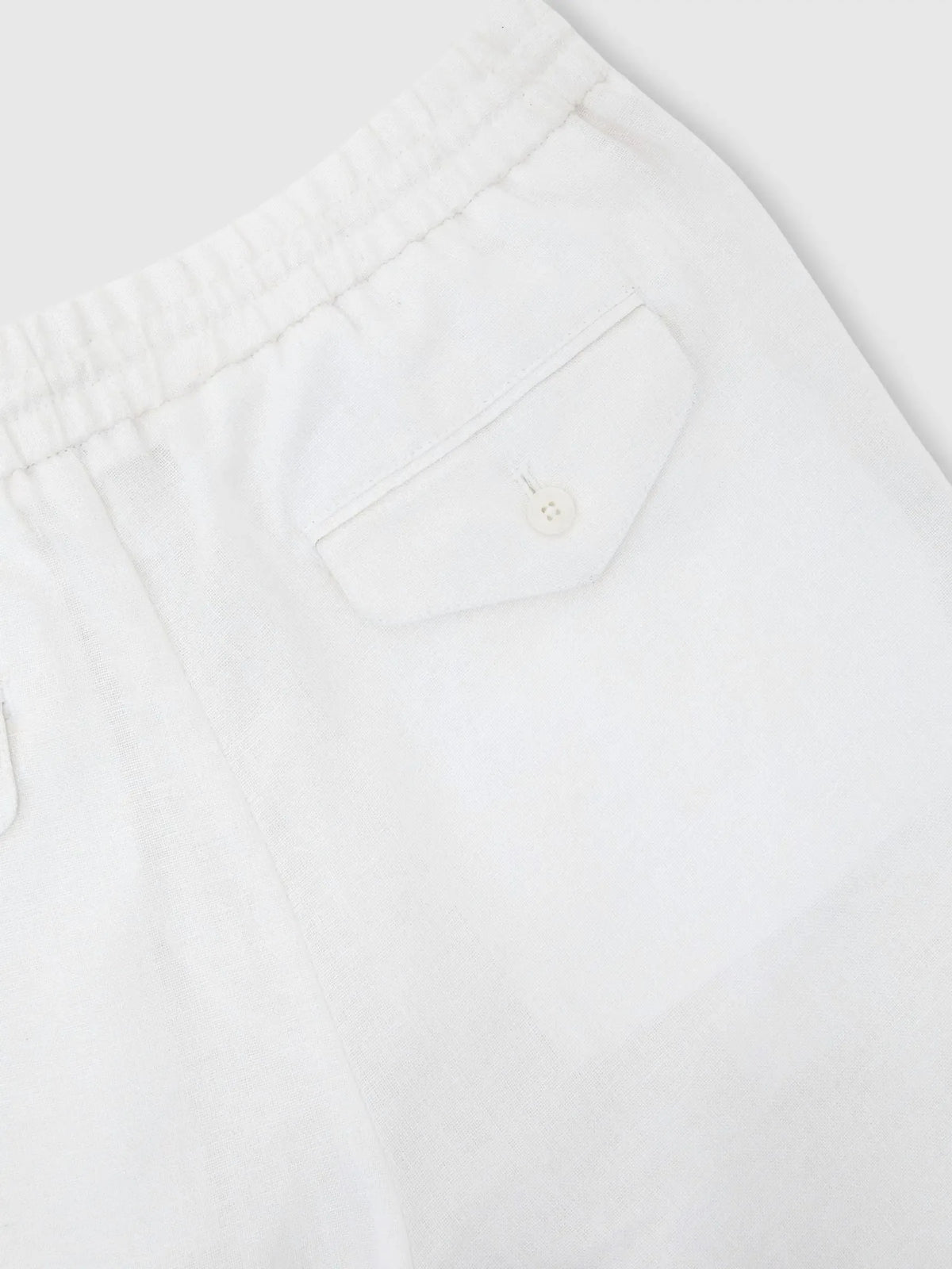 Close-up of back patch pocket with button closure on white linen trousers