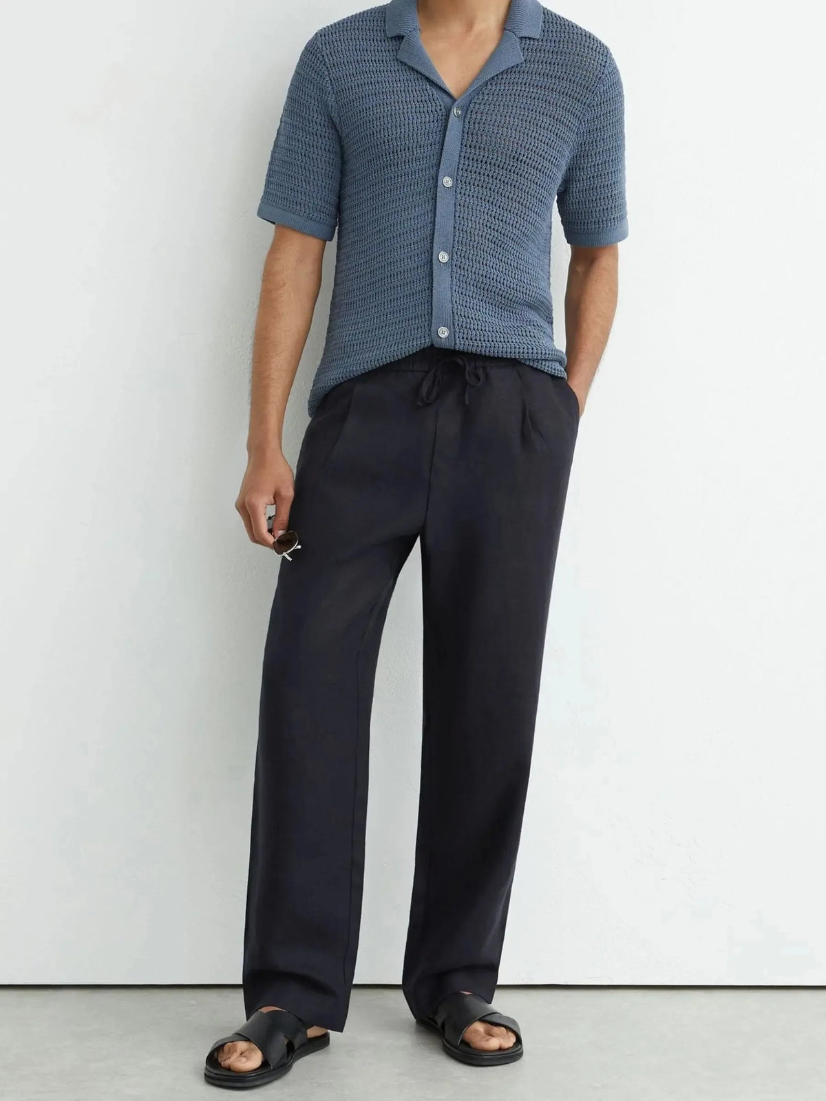Full length front view of man wearing navy linen trousers with knitted polo and black sandals