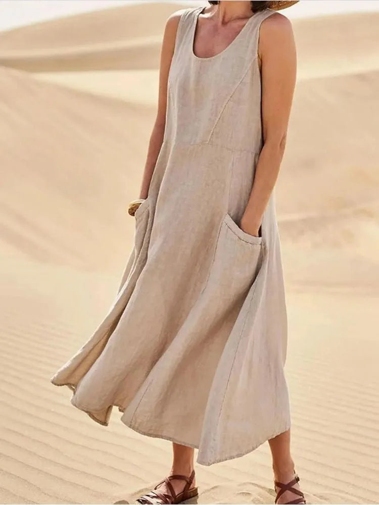 Khaki linen sleeveless midi dress with scoop neck and front pockets, worn walking across sand dunes
