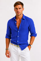 Model wearing a vivid blue linen shirt with white buttons and a neat collar, sleeves rolled, worn with white chino pants.