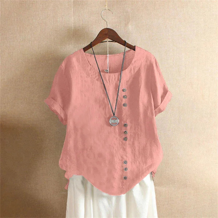 Pink linen short-sleeve blouse on a wooden hanger, showing the round neckline and vertical row of decorative buttons