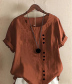 Rust-orange linen blouse on a hanger, paired with a long pendant necklace, showing fabric texture and drape