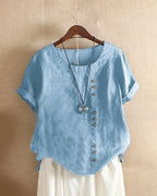 Light blue linen blouse on a wooden hanger, showing the curved hem and relaxed, breathable silhouette