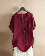 Burgundy linen blouse on a hanger, full view showing the curved hem and short cuffed sleeves