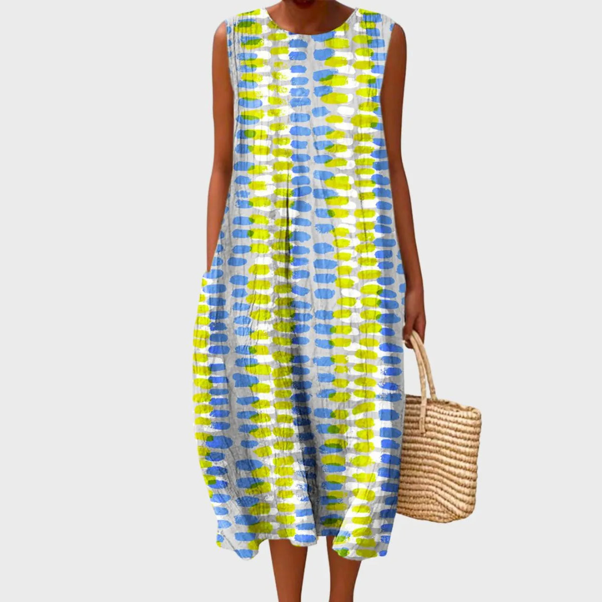 Sleeveless midi dress with a blue and yellow dash print, tiered loose silhouette paired with a straw tote bag