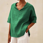 Green linen V-neck top with a relaxed collar, shown on a model with one hand tucked in a white trouser pocket