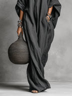 Detail shot of the dress's side pocket and batwing sleeve drape, with the model's hand resting inside the pocket