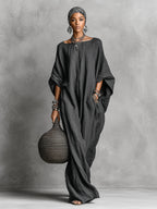 Full-length front view of the dark grey loose maxi dress paired with open sandals, showing the garment's floor-skimming hem