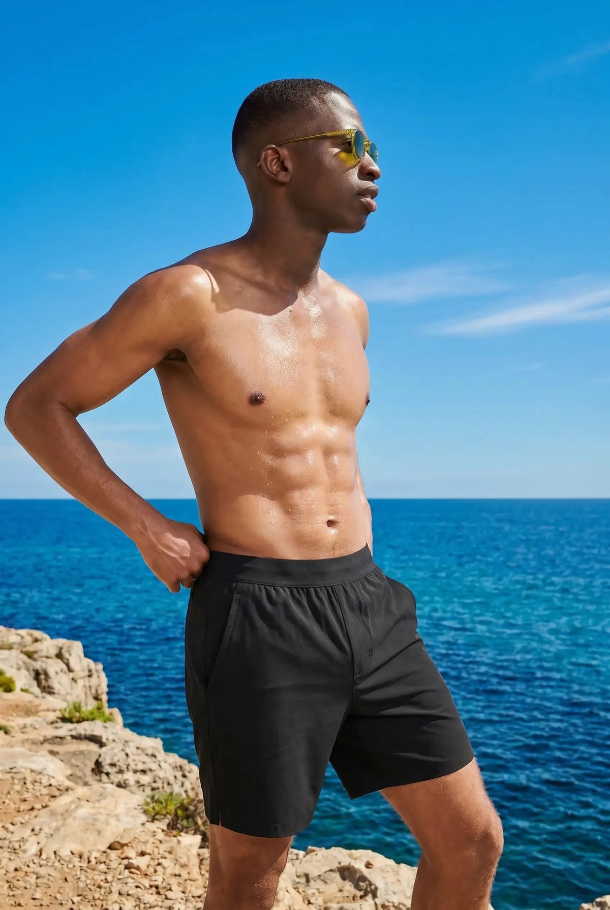 Man in black active shorts standing on coastal rocks overlooking the ocean, showing relaxed above-knee length