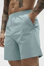 Close-up of pale sage green active shorts showing hand in side pocket and elastic drawstring waistband