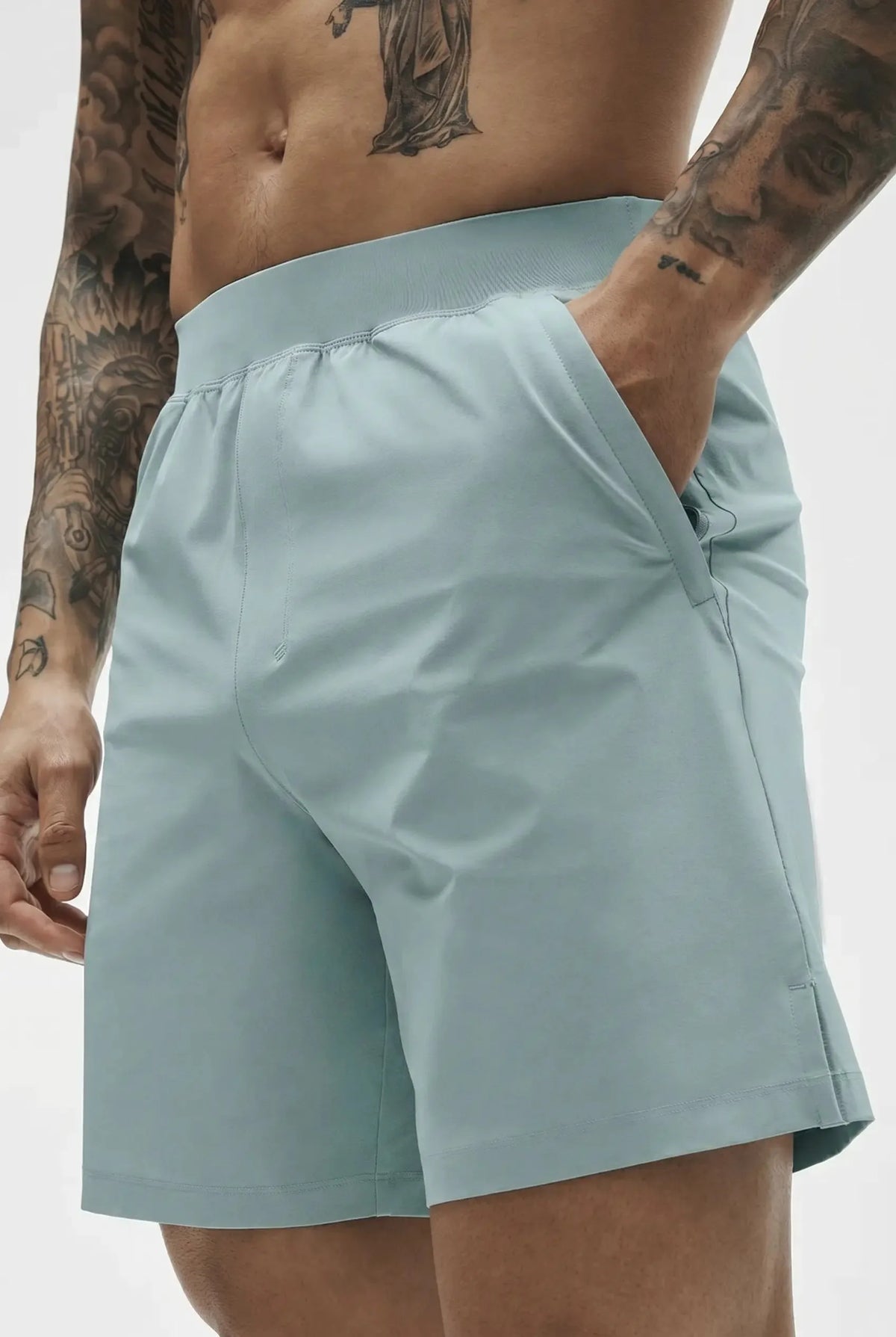 Close-up of pale sage green active shorts showing hand in side pocket and elastic drawstring waistband