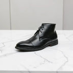 Side view of a black leather chukka boot with cap toe and lace-up front, shown on a marble surface