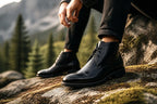 Close-up of a man wearing black leather chukka boots while sitting on a mossy rock outdoors
