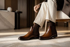 Close-up of brown leather Chelsea boots worn with cream trousers and brown socks indoors