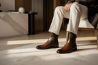 Side view of brown leather Chelsea boots paired with cream tailored pants on a textured rug