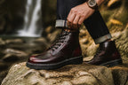 Close-up of a burgundy leather boot on a rock, showing the lace-up front and ridged black rubber sole.