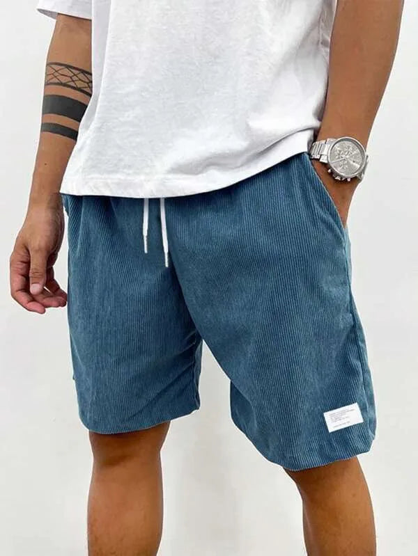 Front view of man wearing teal blue ribbed corduroy shorts with white drawstring and white t-shirt