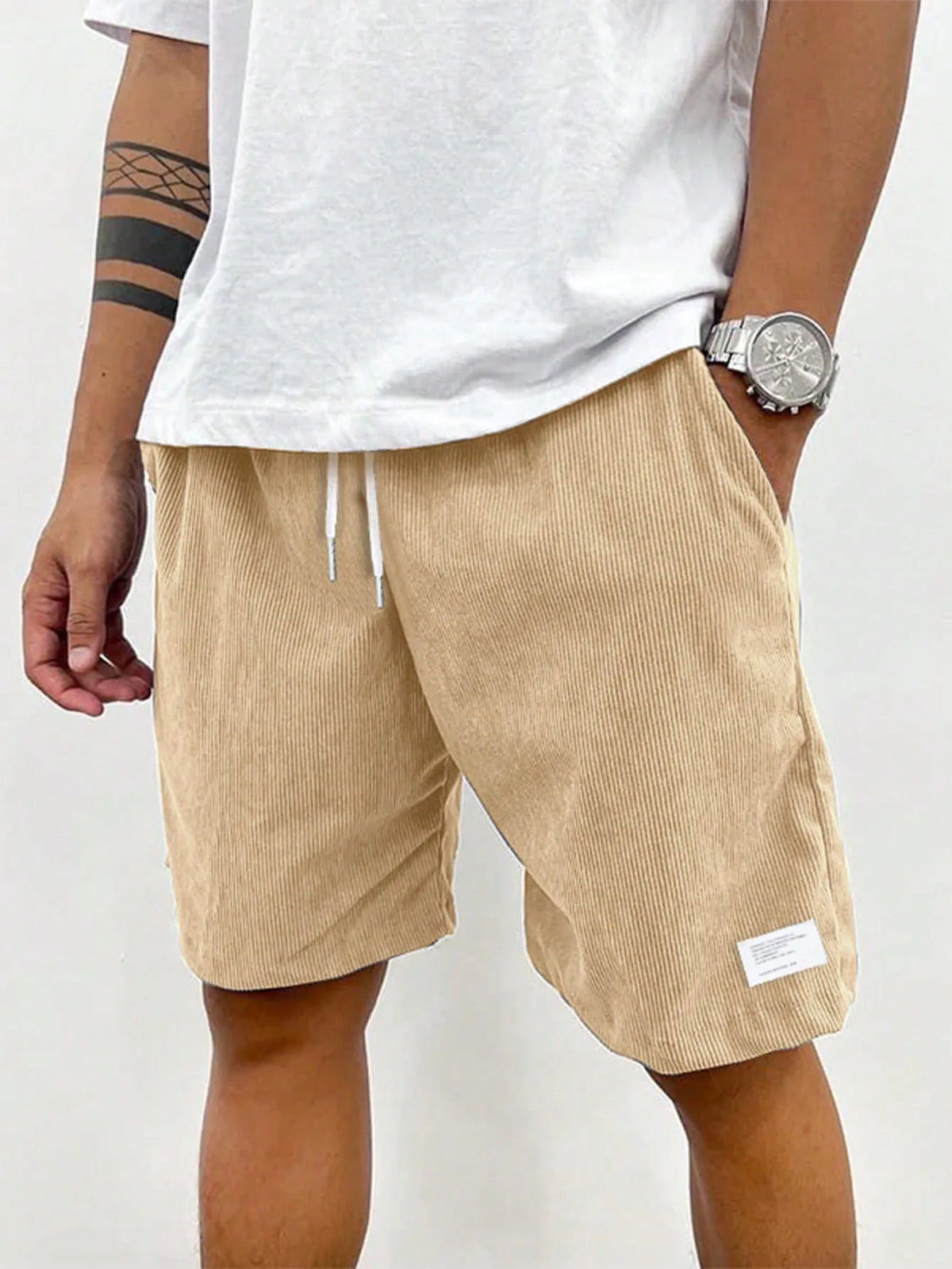 Front view of beige ribbed corduroy shorts worn with white t-shirt and silver watch