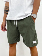 Close-up of teal blue corduroy shorts showing woven fabric label near hem