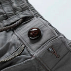 Close-up of grey shorts front button closure with brown button and drawstring cord