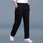 Front view of black jogger pants with drawstring waist, zip side pocket and tapered fit, worn with white sneakers.