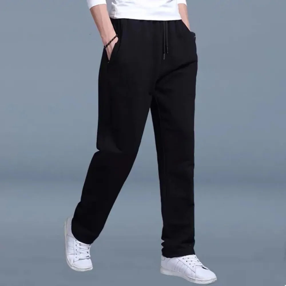 Front view of black jogger pants with drawstring waist, zip side pocket and tapered fit, worn with white sneakers.