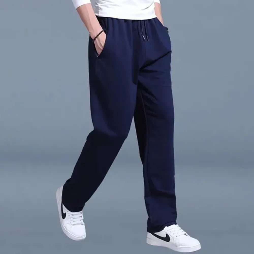 Side view of navy jogger pants showing slim tapered leg and elastic drawstring waistband, paired with white Nike sneakers.
