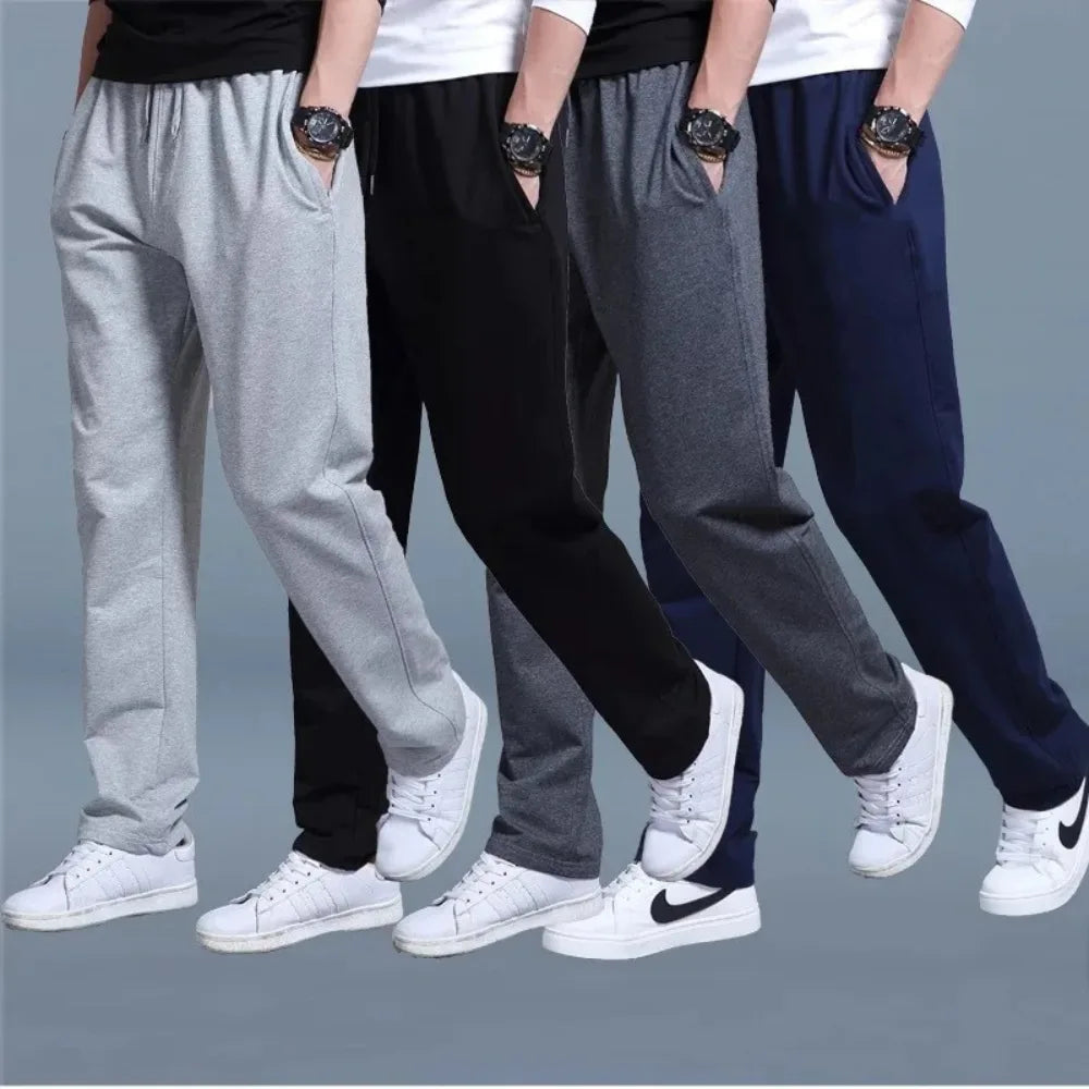 Four men standing side by side wearing the jogger pants in light grey, black, charcoal grey and navy.