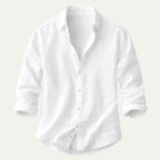 Flat lay of a white cotton-linen button-up shirt with rolled sleeves on a plain background