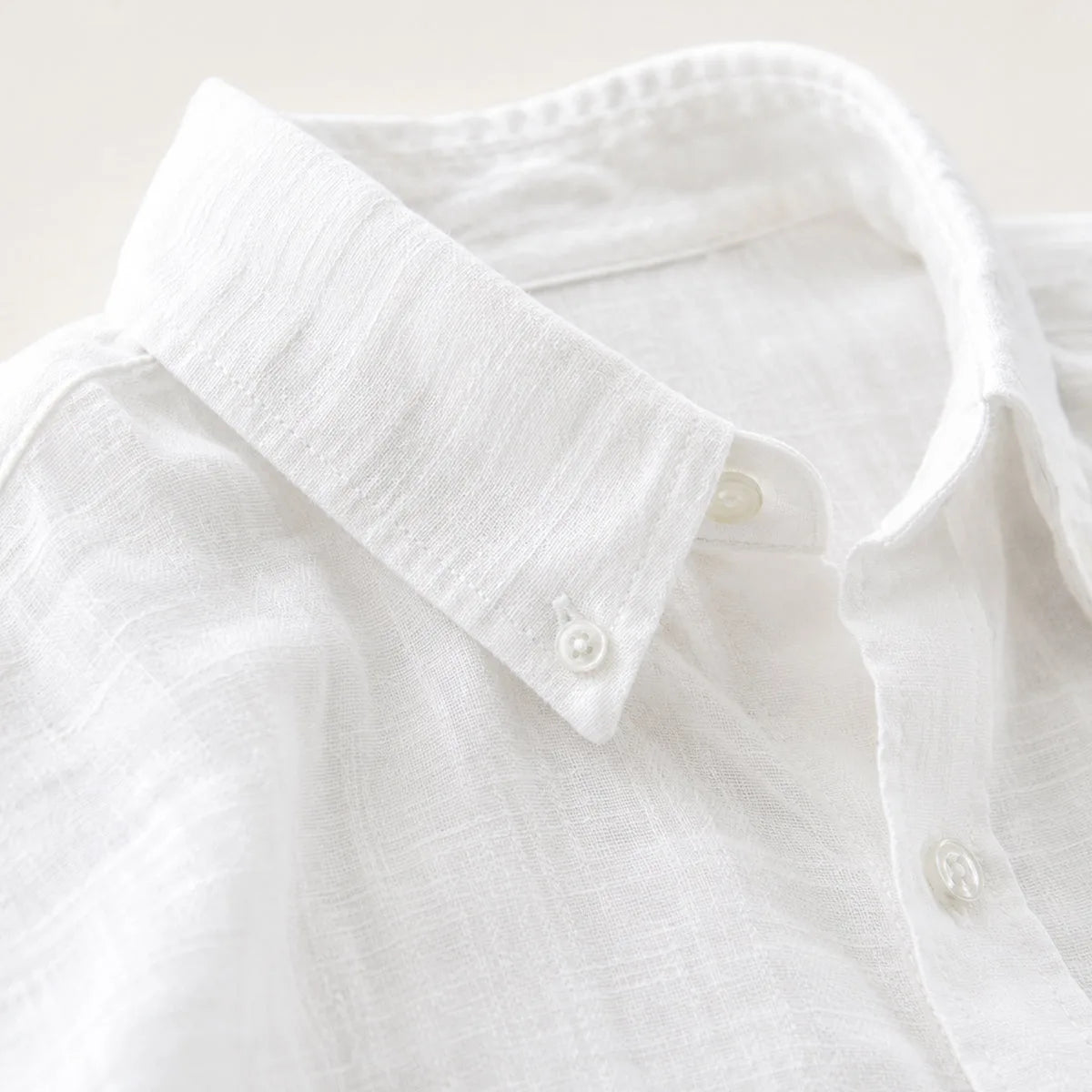 Close-up of the white shirt's collar and mother-of-pearl buttons showing the woven linen texture