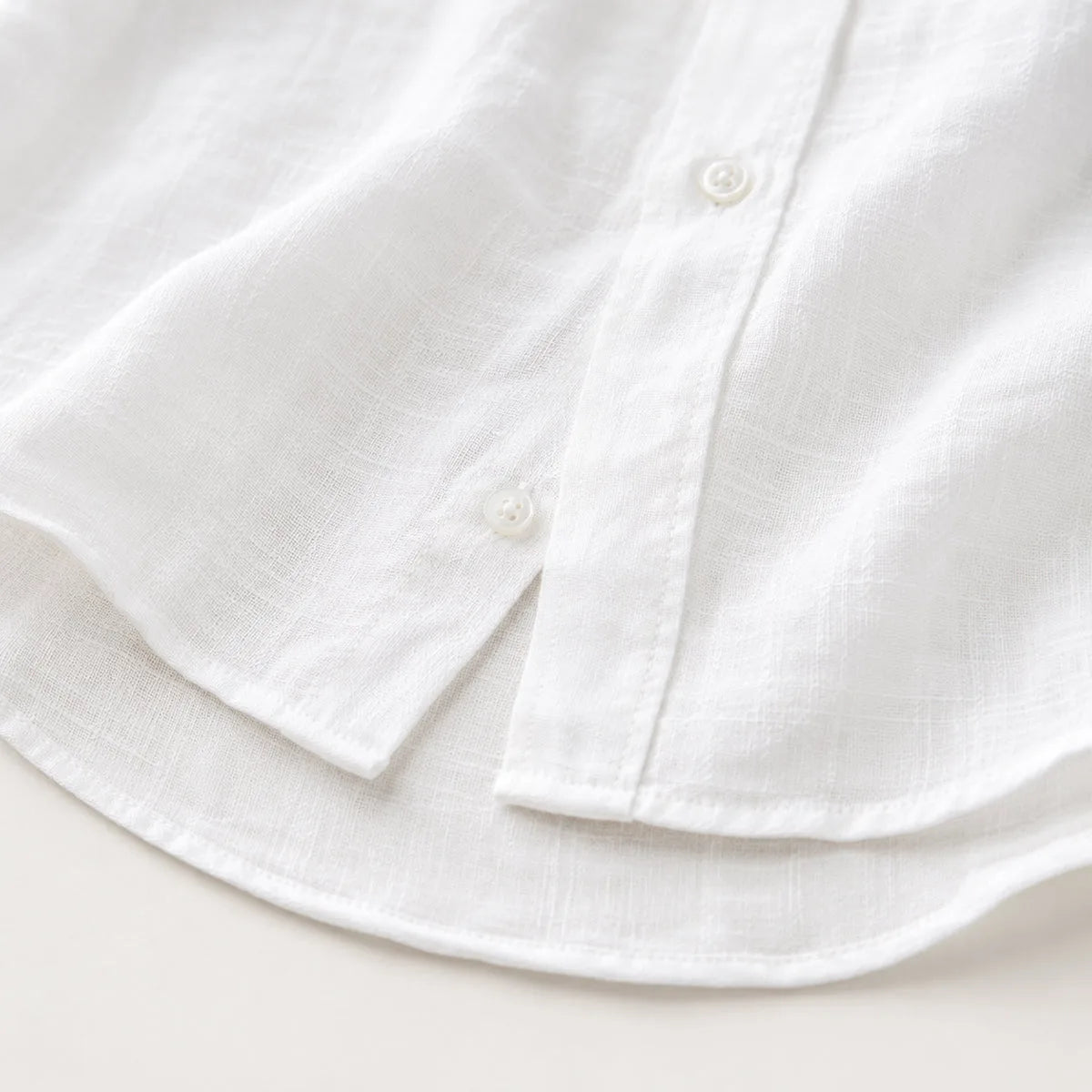 Close-up of the white shirt's curved hem and side button placket detailing