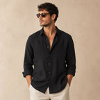 Man wearing a black linen button-up shirt open at the collar styled with white pants